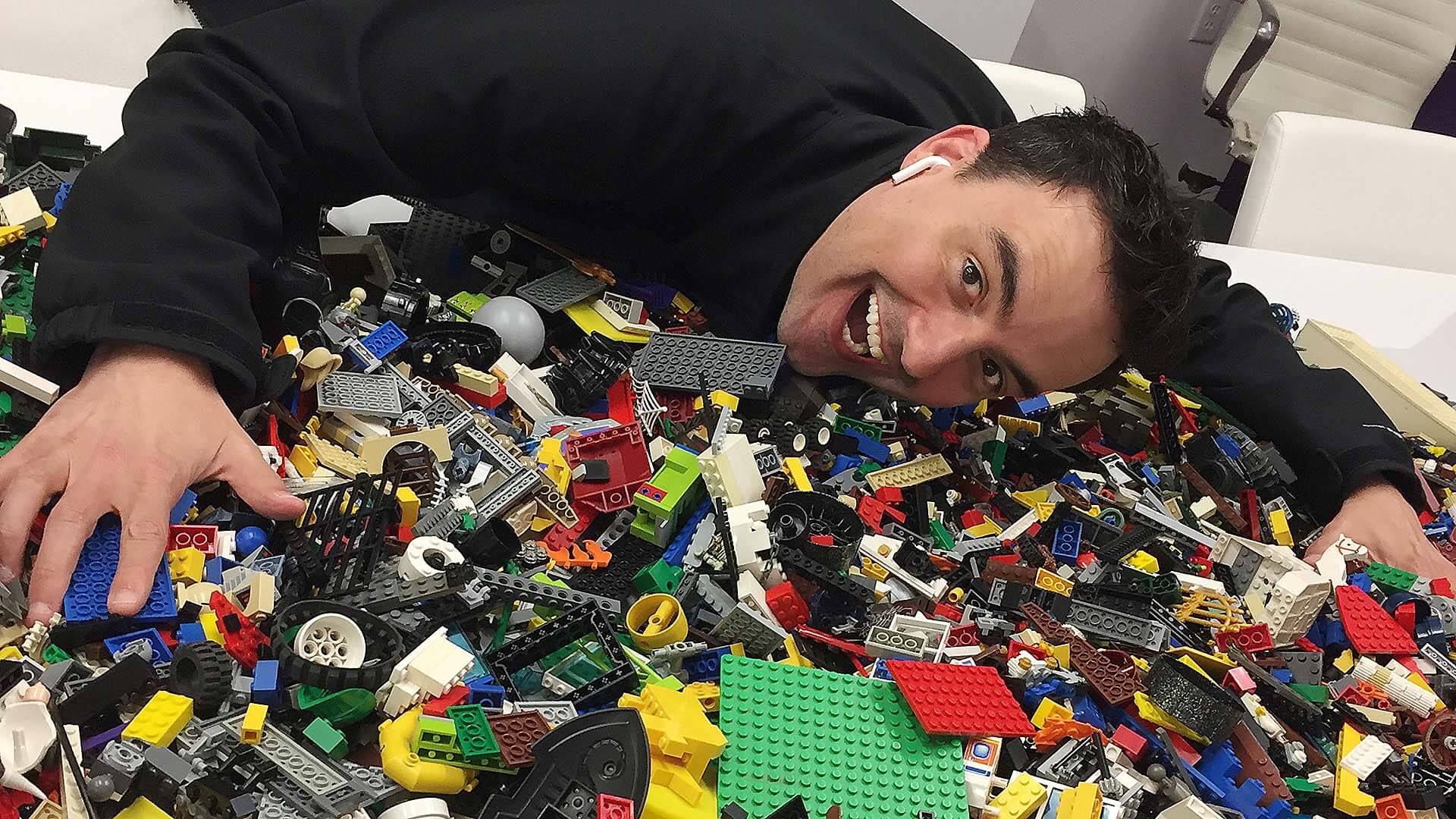 isral Duke leaning over a pile of Legos. He has a large smile and excited facial expression.